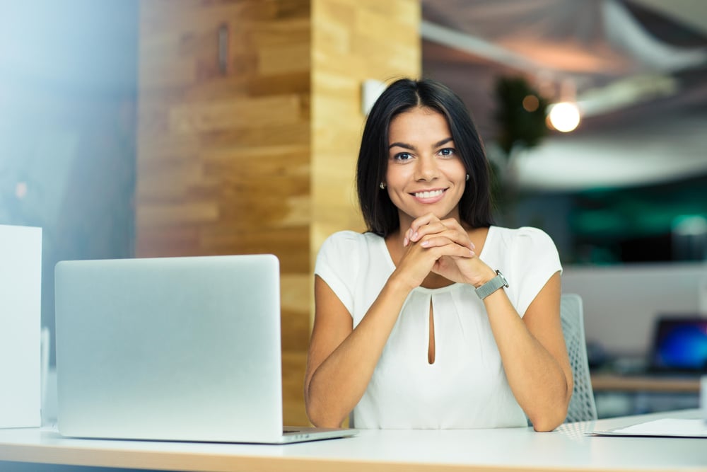 Portrait of a cheerful businesswoman sitting at the table in office and looking at camera Portrait of a cheerful businesswoman sitting at the table in office and looking at camera
